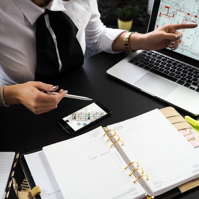 A business professional working on real estate project plans using multiple devices in an office setting.